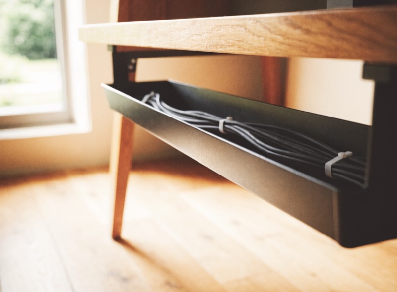 A cable tray mounted under a wooden desk holding bundled cables