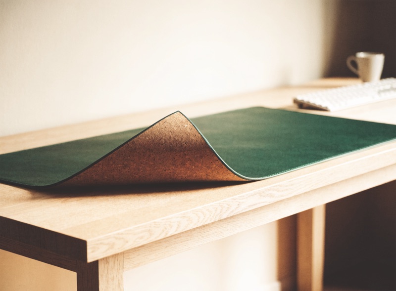A large felt and cork desk mat across a pale oak desk