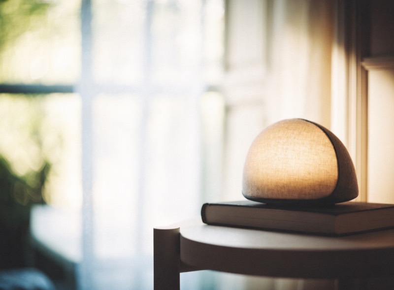 A dome-shaped sunrise alarm clock glowing amber on a bedside table